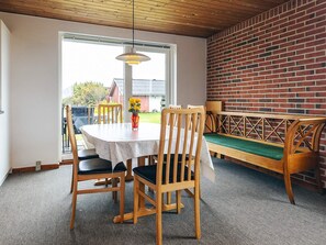 A dining area with a round table, wooden chairs, a bench with a green cushion, and a brick wall.