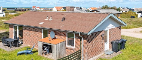 A single-story brick house with a sloped roof, a small porch, and a satellite dish.