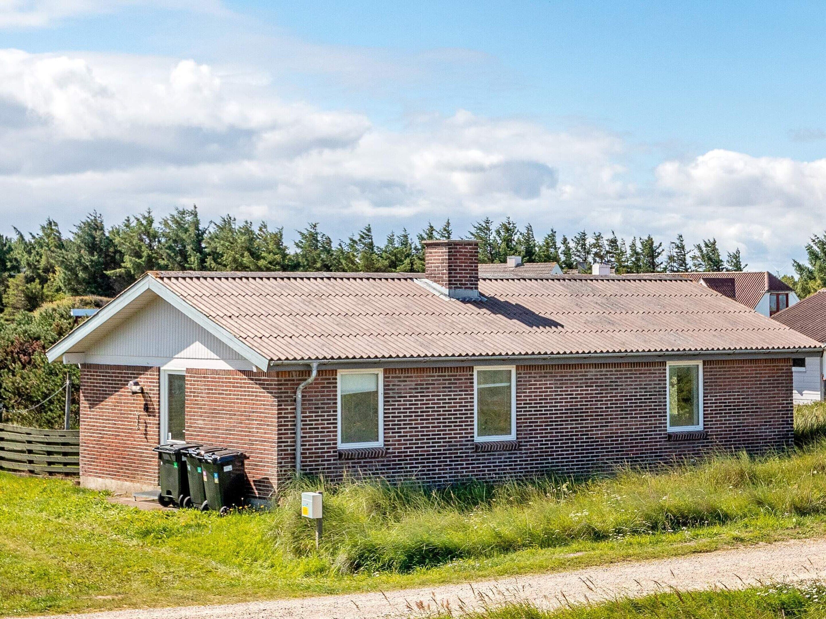 A single-story brick building with a gabled roof, a small attached garage, and a grassy area in front.