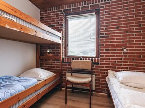 Ett studentrum med två våningssängar, en stol, ett fönster med persienner och en tegelvägg.