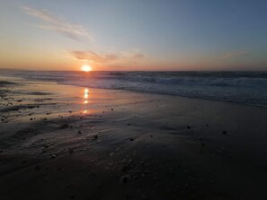 A beach with the sun setting over the horizon, waves gently lapping at the shore.