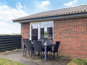 A patio area with a table and chairs, a sliding glass door, and a brick wall. - 7 Person Holiday Home in Frostrup (Frøstrup)