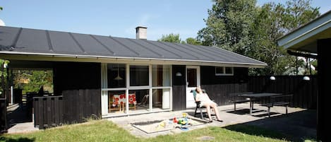 A house with a covered patio, a fenced yard, and a person relaxing on a chair.