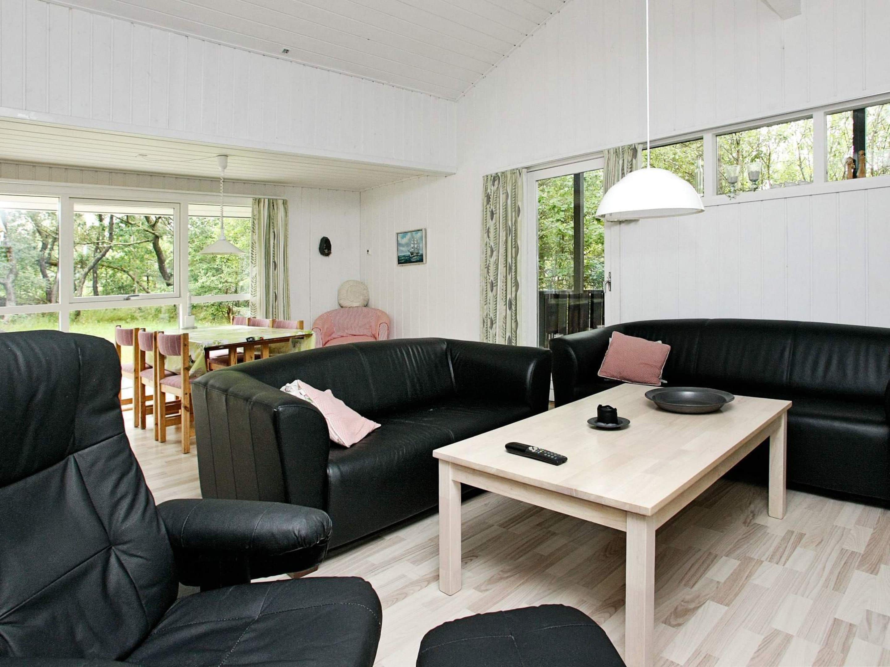 A modern living room with a black leather sofa, a wooden coffee table, and a dining area with a table and chairs.