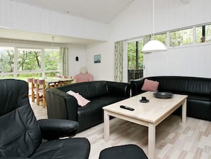 Een moderne woonkamer met een zwarte leren bank, een houten salontafel en een eethoek met een tafel en stoelen.