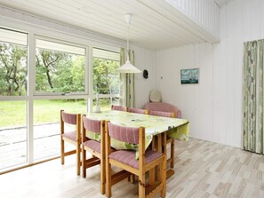 A dining area with a table and chairs, large windows, and a view of greenery outside. - 6 Person Holiday Home in Albaek (Jerup)