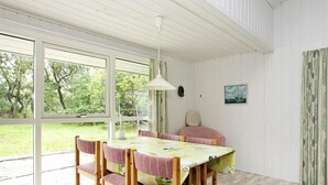 A dining area with a table and chairs, large windows, and a view of greenery outside.