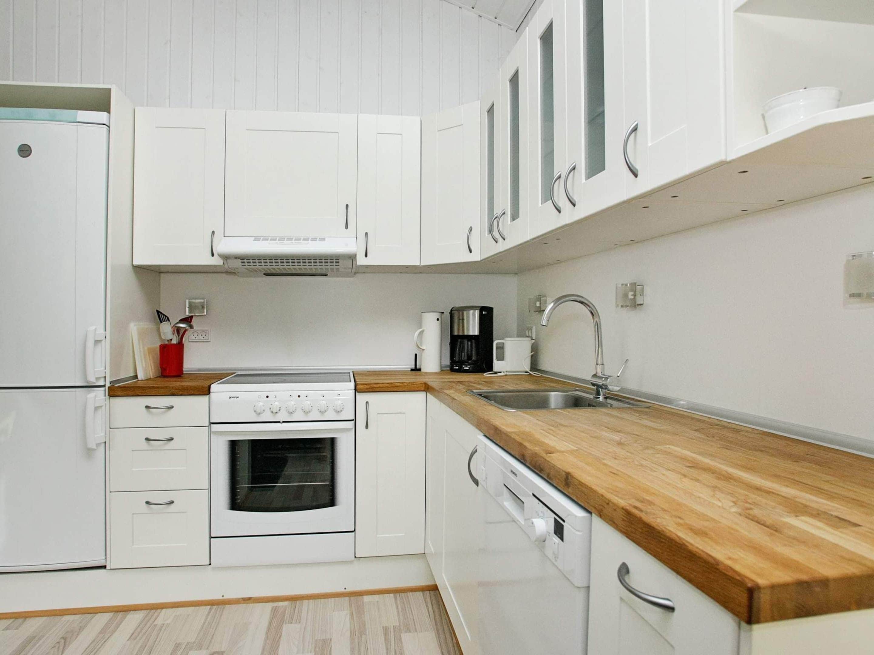 Een moderne keuken met witte kasten, een houten aanrecht, een ingebouwde oven, een koffiezetapparaat en een spoelbak.
