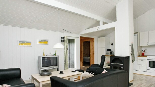 A modern living room with a sofa, a television, a dining table, and a kitchen area with cabinets and a microwave.