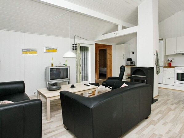A modern living room with a sofa, a television, a dining table, and a kitchen area with cabinets and a microwave.