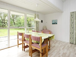 A dining area with a table and chairs, large windows, and a view of greenery outside.