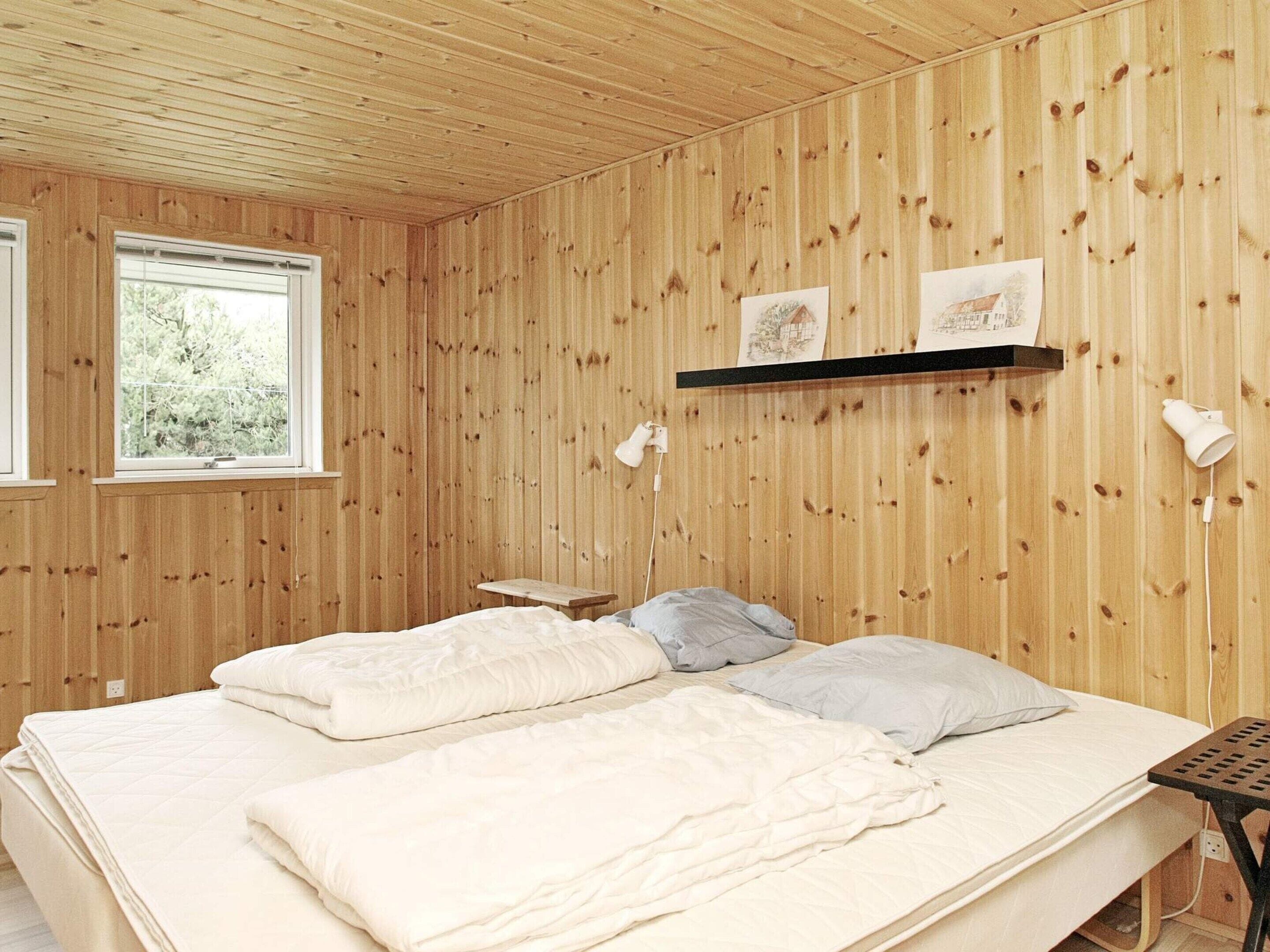 Een kamer met houten paneelwanden, een bed met witte beddengoed, een klein nachtkastje en een raam met uitzicht op groen.