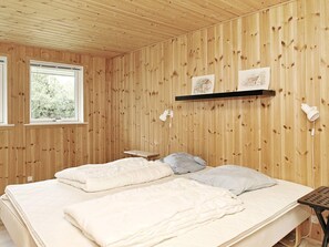 A room with wooden panel walls, a bed with white bedding, a small bedside table, and a window with a view of greenery. - 6 Person Holiday Home in Albaek (Jerup)