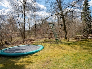 A trampoline in a grassy yard with a swing set and trees in the background.