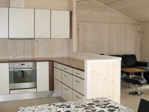 Une cuisine moderne dotée d’un four encastré et de meubles de rangement, un coin repas avec une table et des chaises, et un canapé en cuir noir.