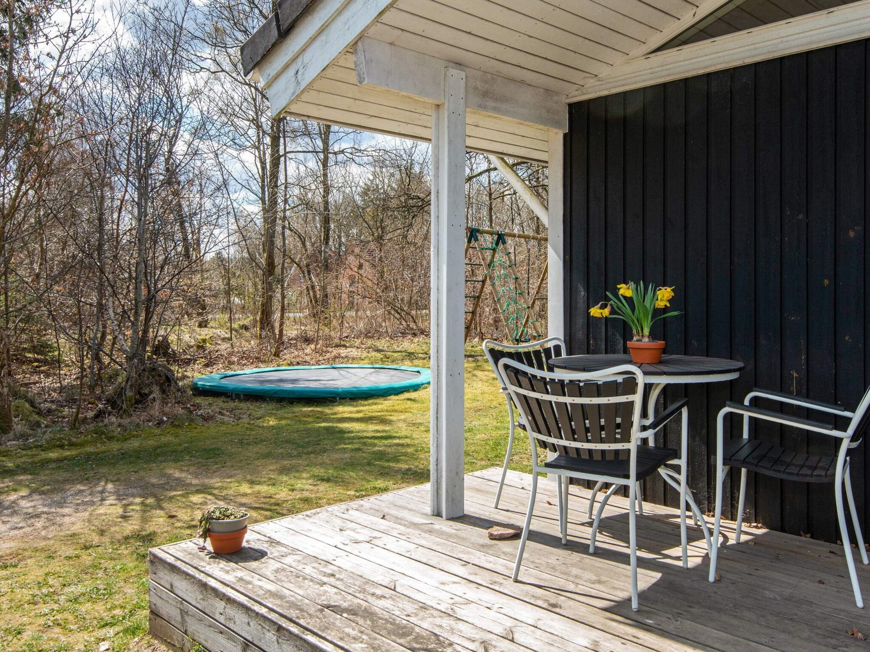 Un espace extérieur abrité, équipé d’une table et de chaises, d’un trampoline et d’une terrasse en bois.
