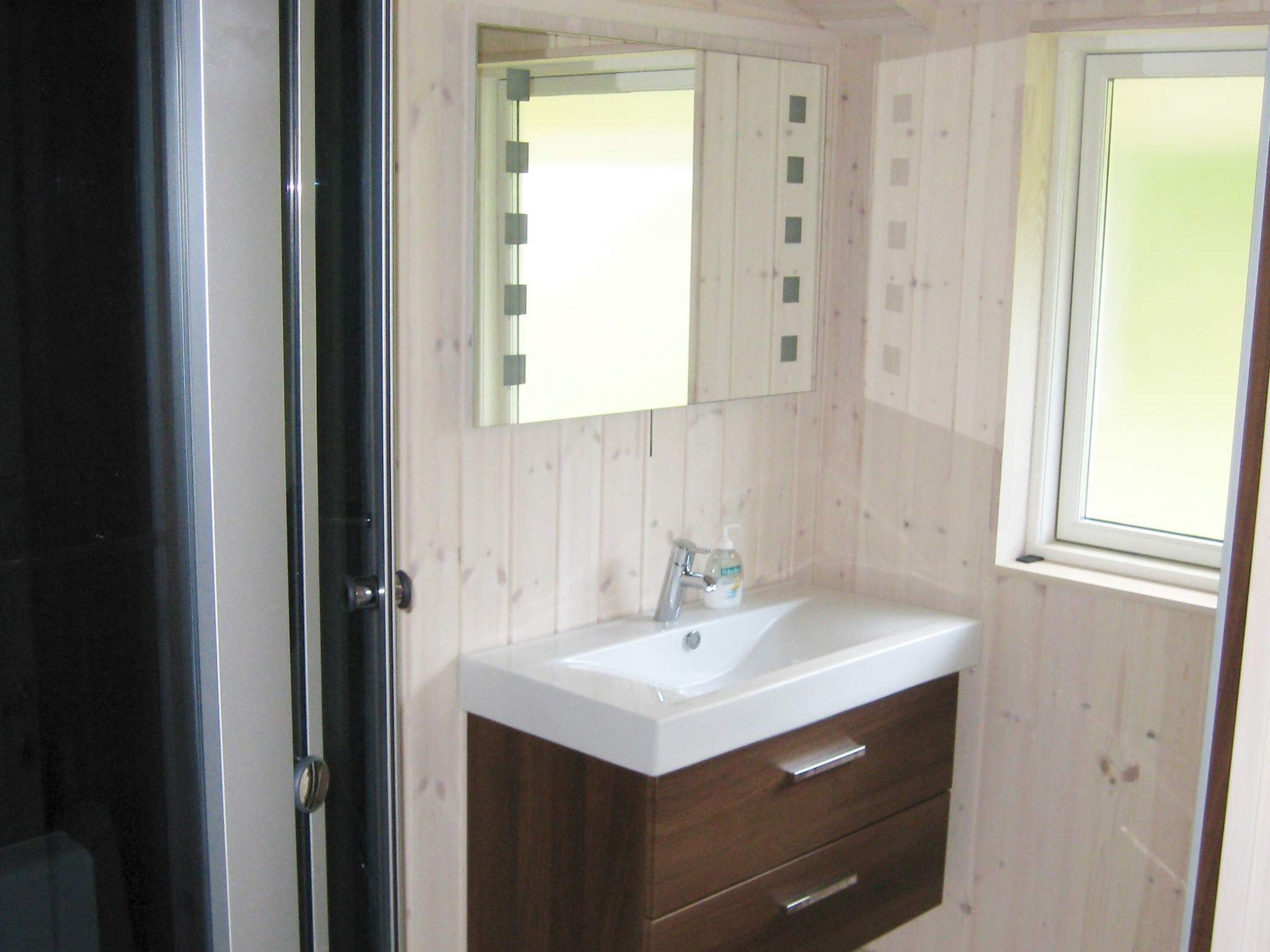 A bathroom with a white sink, a mirror, and a window.