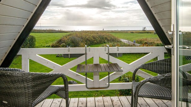 A balcony with wicker chairs, a wooden table, and a view of the sea and grassy fields. - Seaside Spa Retreat - By Traum Ferienwohnungen (Haderslev)