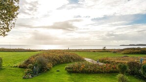 A coastal landscape with a grassy field, a small path, and a bench. - Seaside Spa Retreat - By Traum Ferienwohnungen (Haderslev)