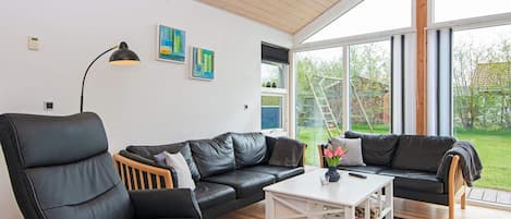 A modern living room with a black leather sofa, a white coffee table, and a large window providing a view of the outdoors.