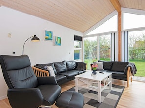 A modern living room with a black leather sofa, a white coffee table, and a large window providing a view of the outdoors.