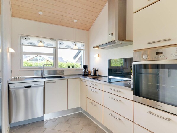 A modern kitchen with a dishwasher, oven, and a window with blinds.
