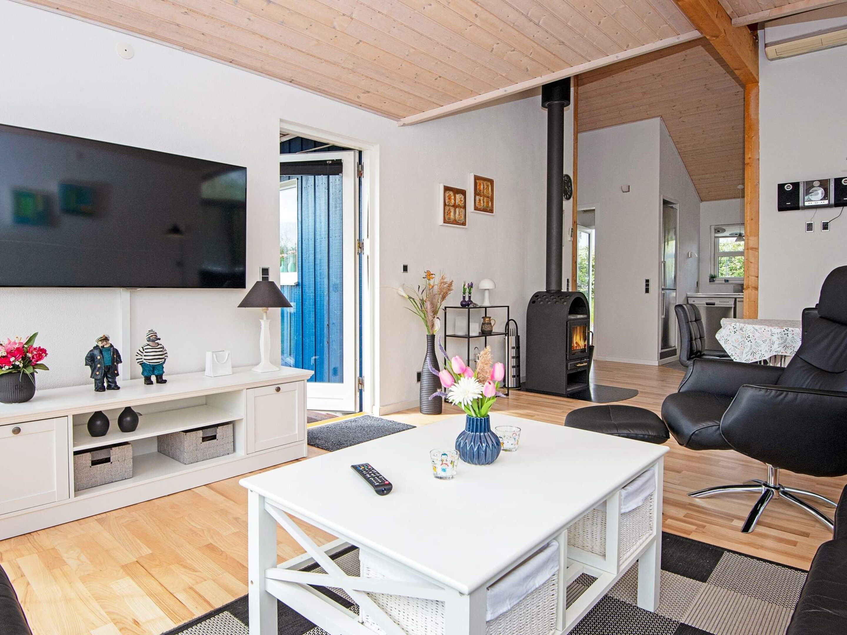 A modern living room with a flat-screen TV, a fireplace, a dining area, and a black leather chair.