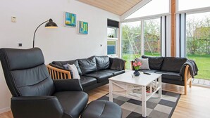 A modern living room with a black leather sofa, a white coffee table, and a large window offering a view of the outdoors.