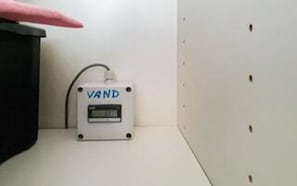 A white device labeled 'VAND' on a white wall with a black object to its left.
