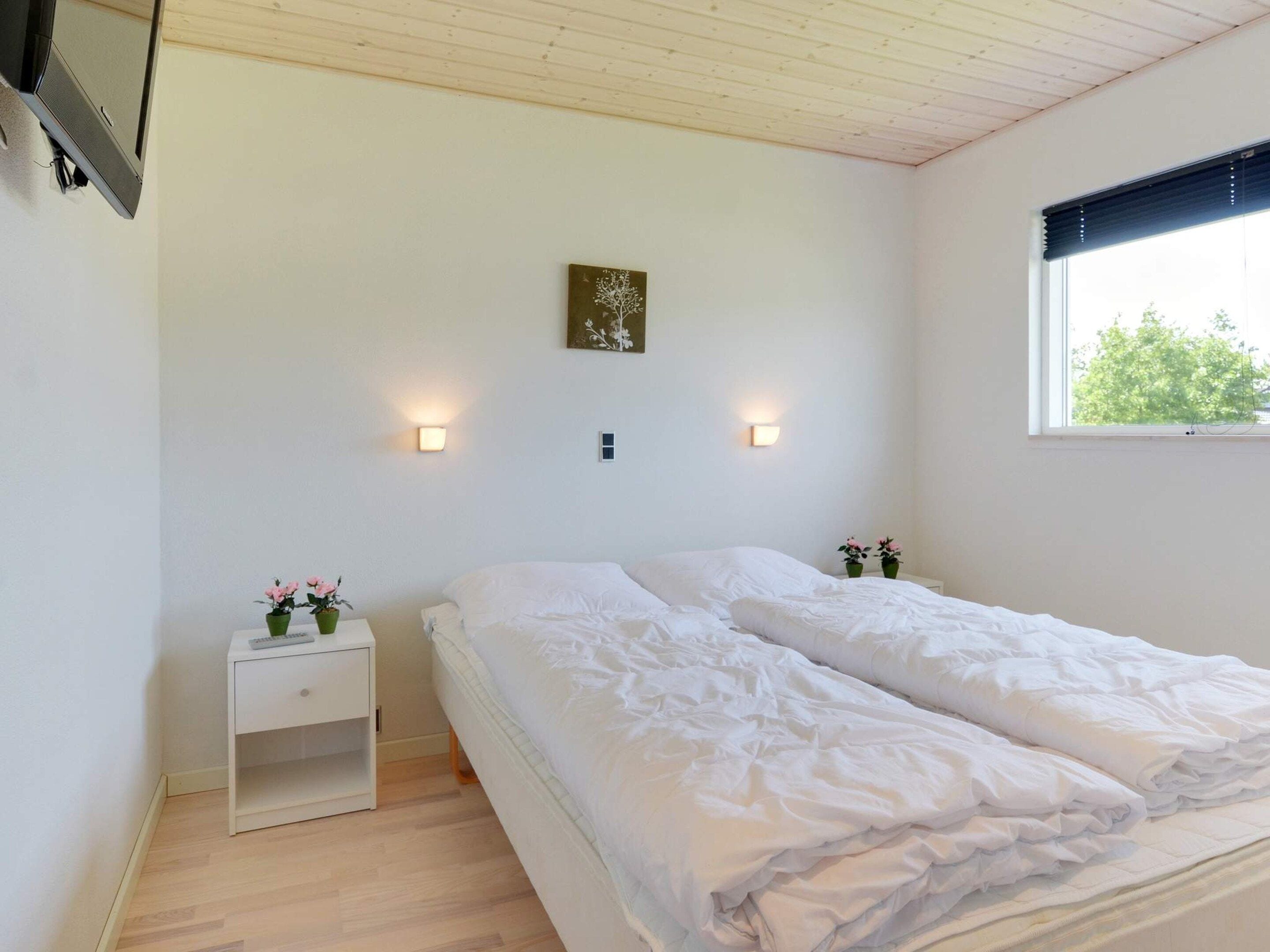 A bedroom with two beds, a nightstand, a wall-mounted TV, and a window with a view of trees.
