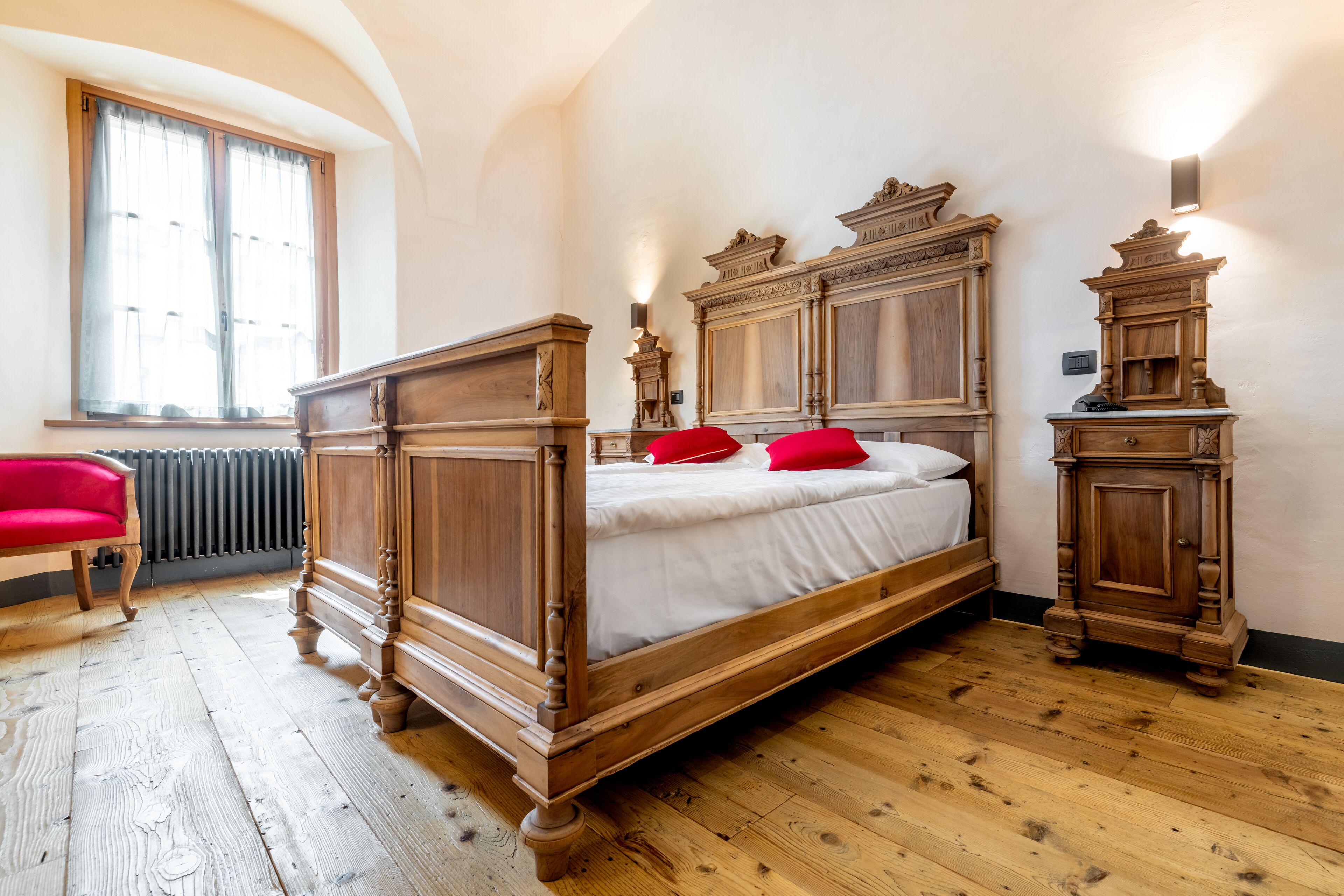 A bedroom with a wooden four-poster bed, a red chair, and a radiator.