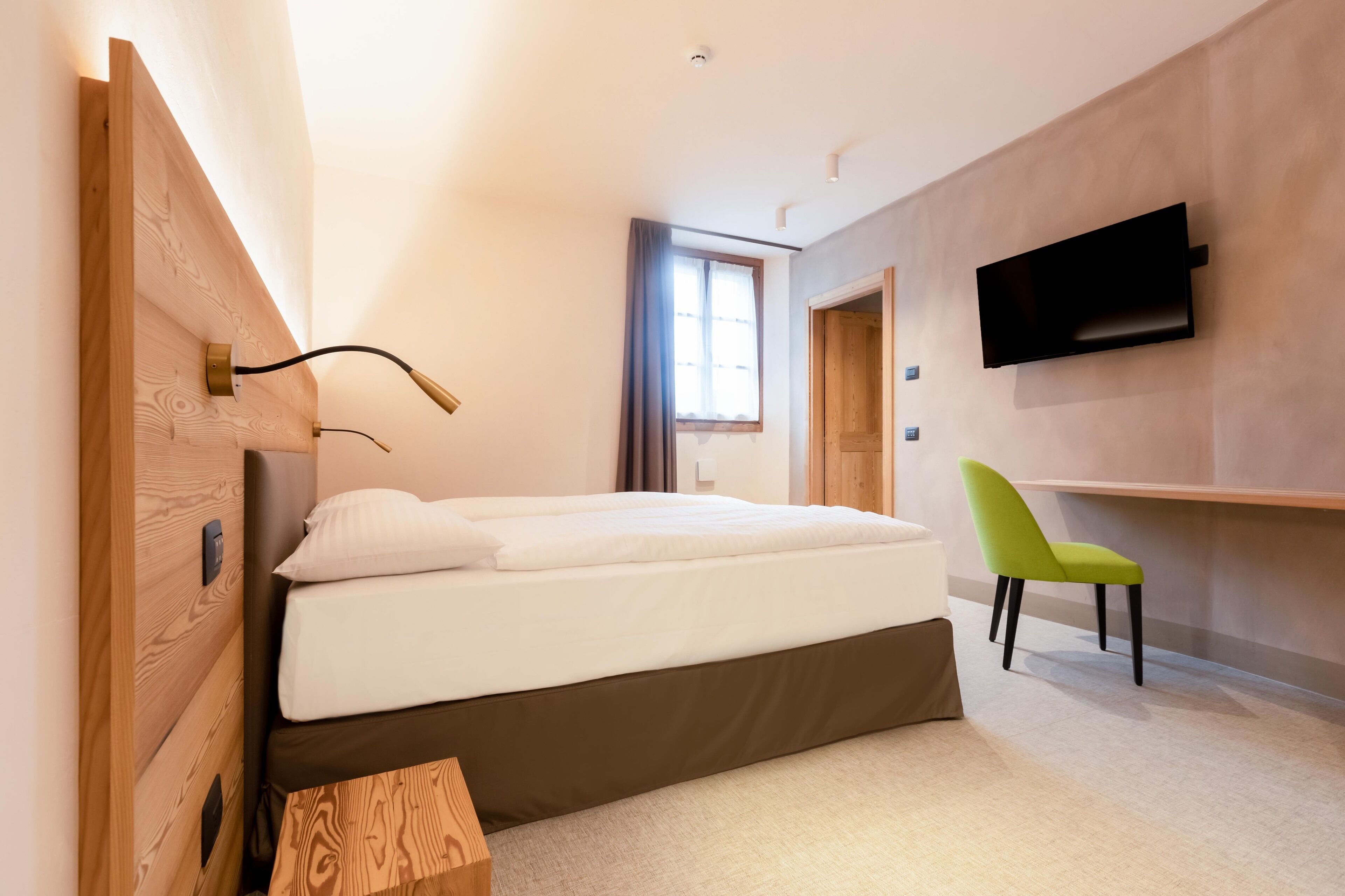Un dormitorio moderno con una cama, un escritorio, una silla y un televisor instalado en la pared.