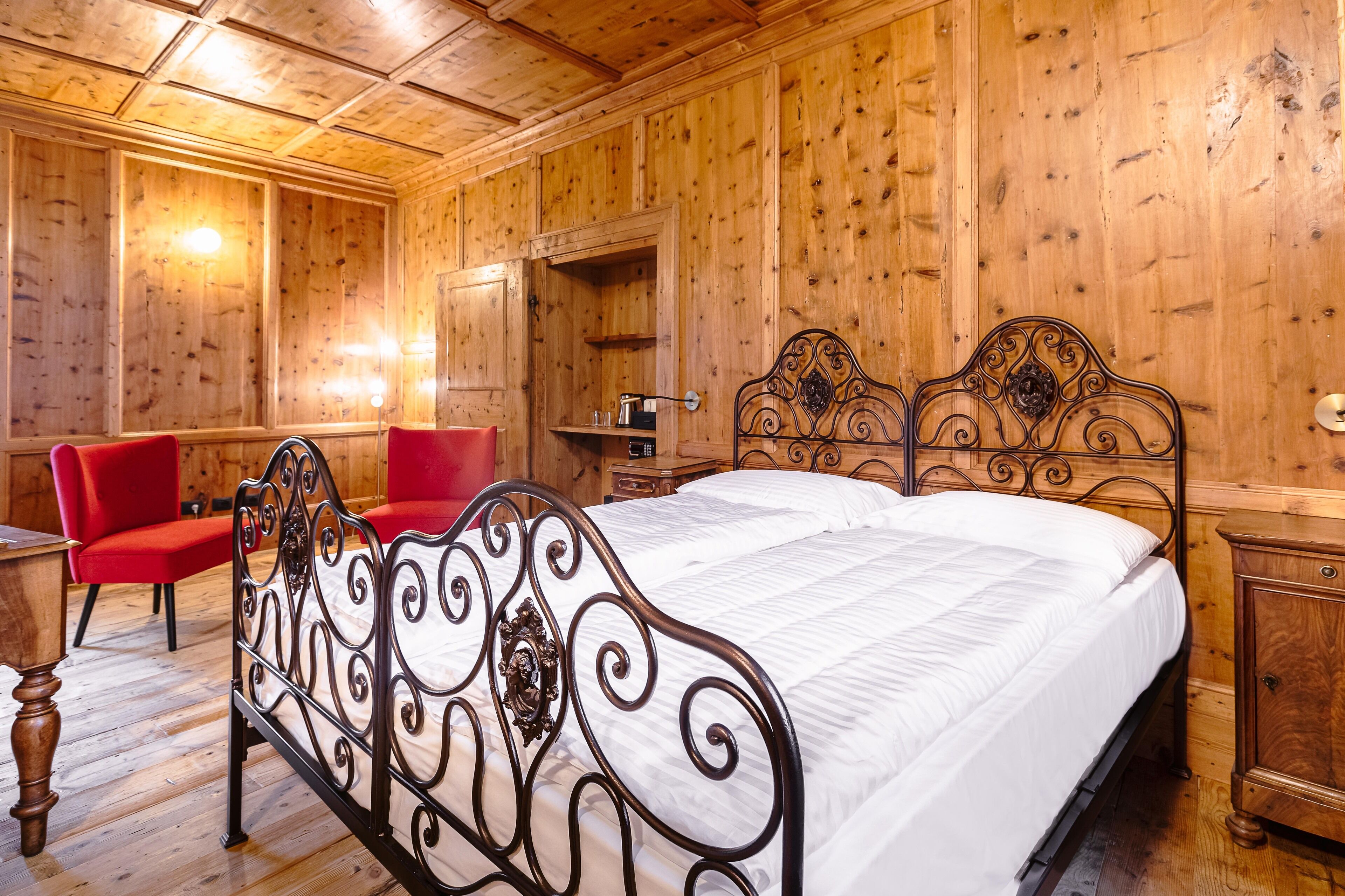 Una habitación con paneles de madera, un marco de cama de metal, una silla roja y un armario de madera.