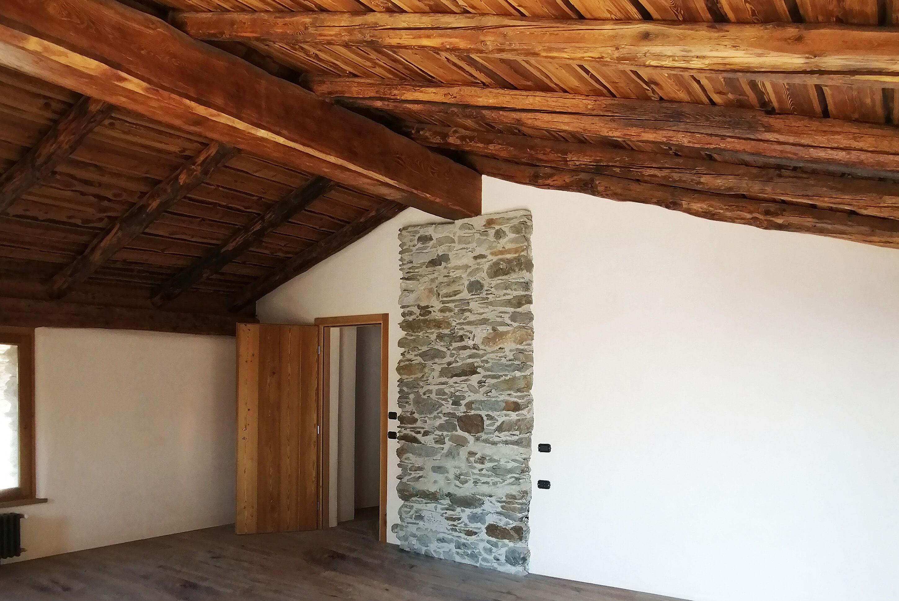 Una habitación con techo de madera, pared de piedra y puerta de madera.