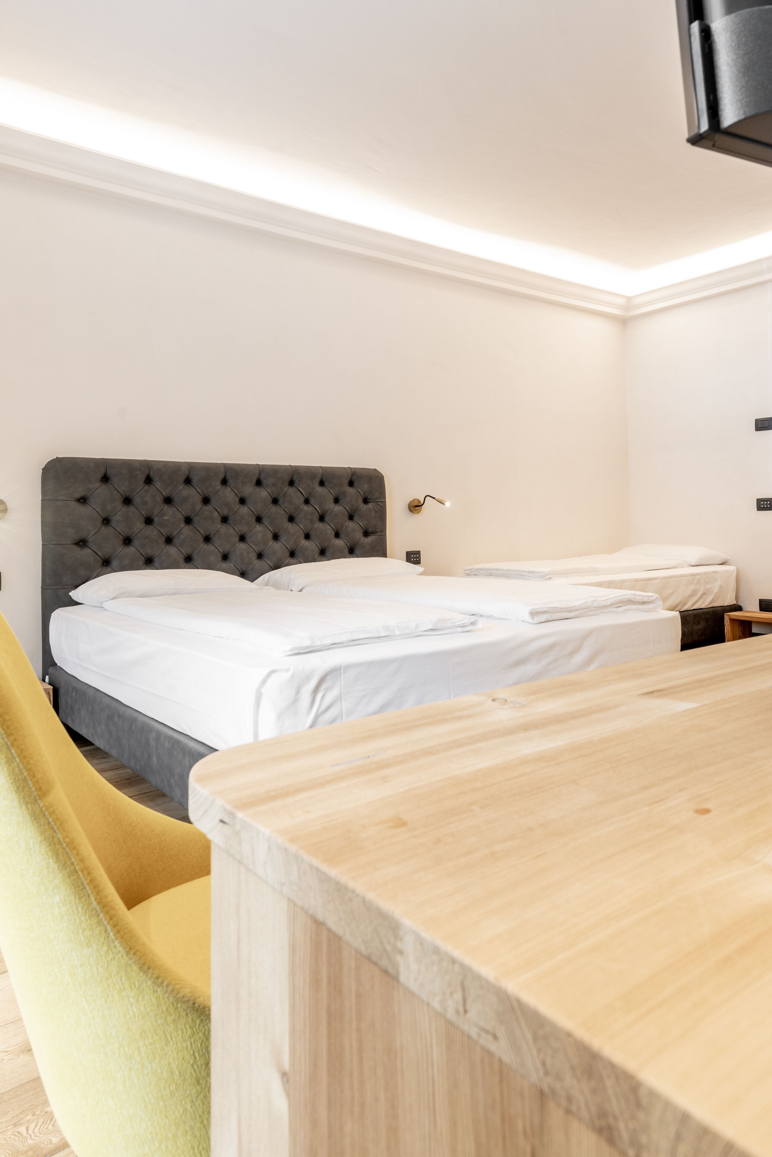 Habitación de hotel con una cama grande, una cama más pequeña, una mesa de madera y una silla amarilla.