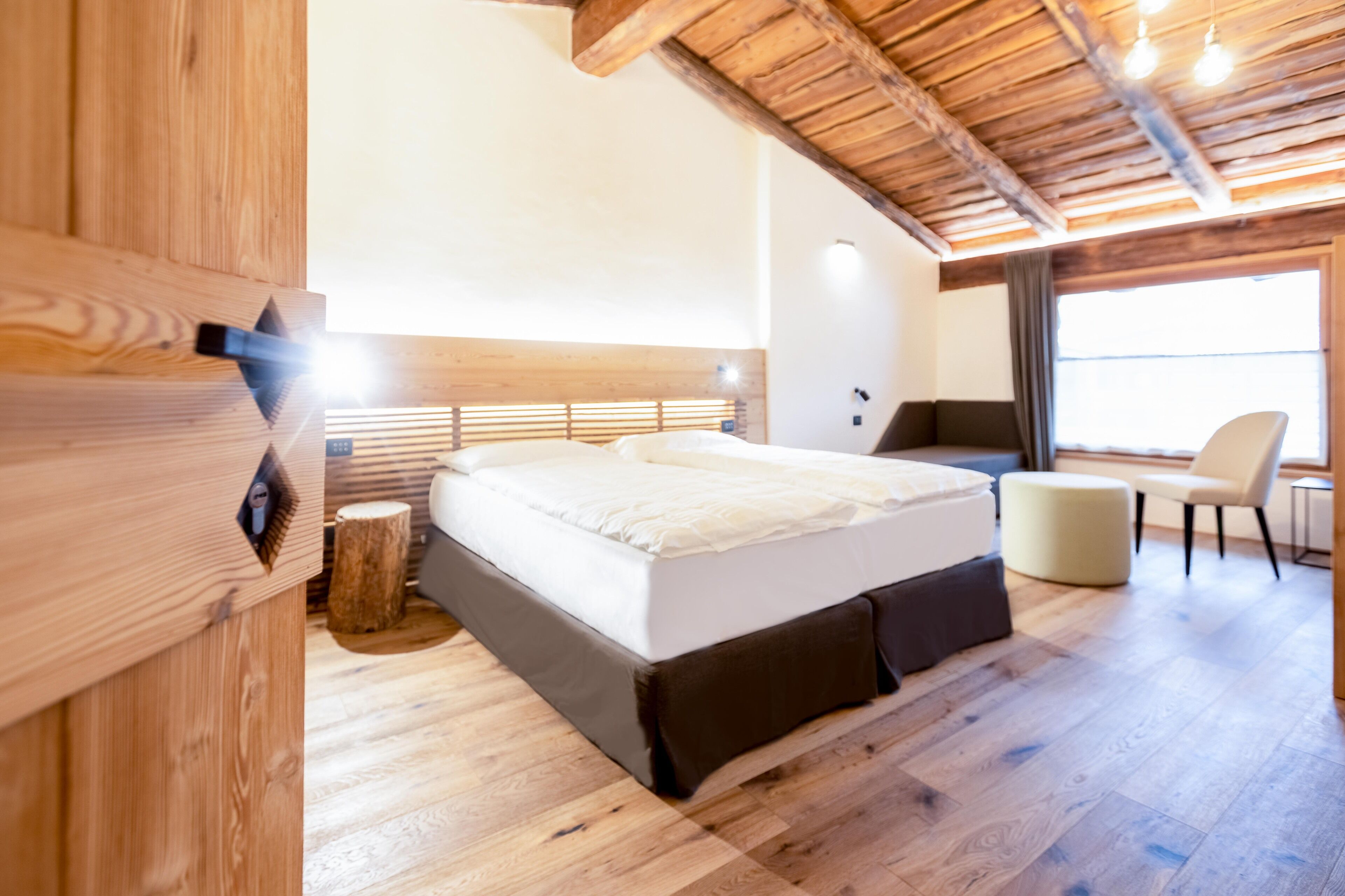 A modern bedroom with a wooden ceiling, a large bed, a chair, and a window.
