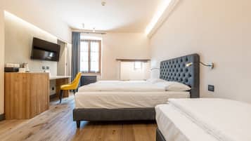Ein Hotelzimmer mit zwei Betten, einem Schreibtisch mit Stuhl, einem an der Wand montierten Fernseher und einem Fenster mit Vorhängen.
