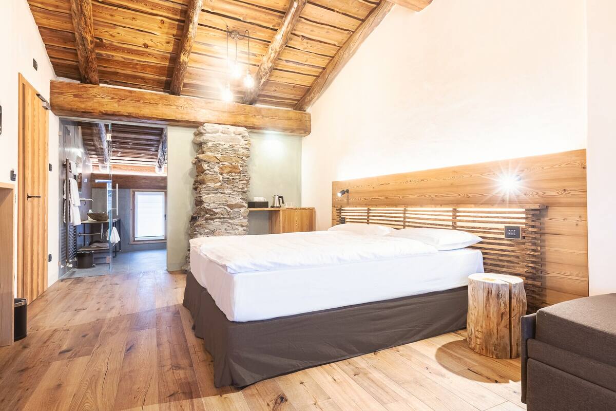 Ein Schlafzimmer mit Holzbalkendecke, Steinwand und einem Bett mit Kopfteil.