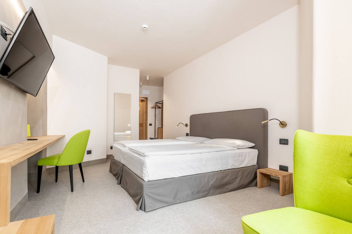 Ein modernes Schlafzimmer mit einem Bett, einem Schreibtisch, einem Stuhl und einem an der Wand montierten Fernseher.