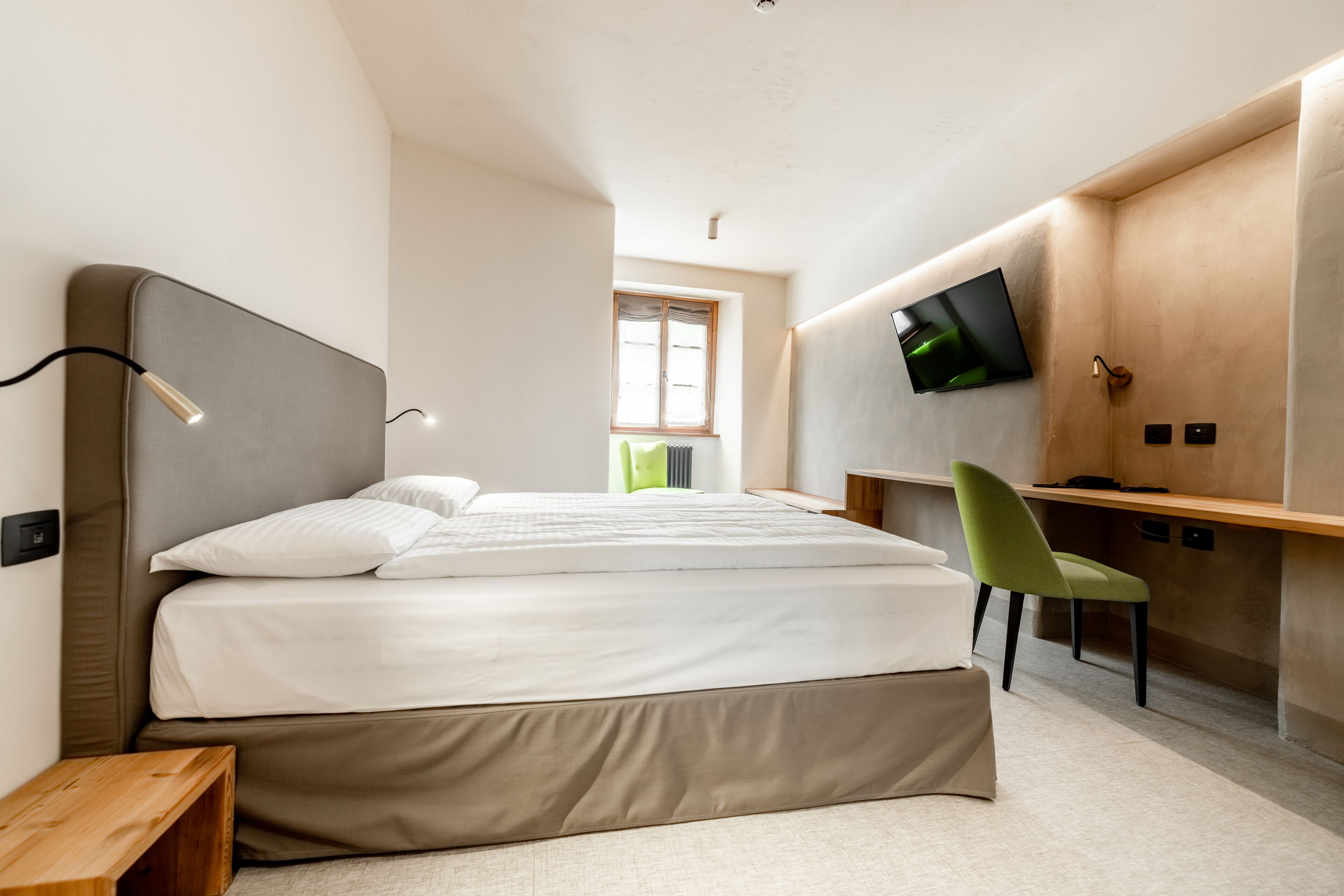 A modern bedroom with a bed, a desk, a chair, a TV, and a window.