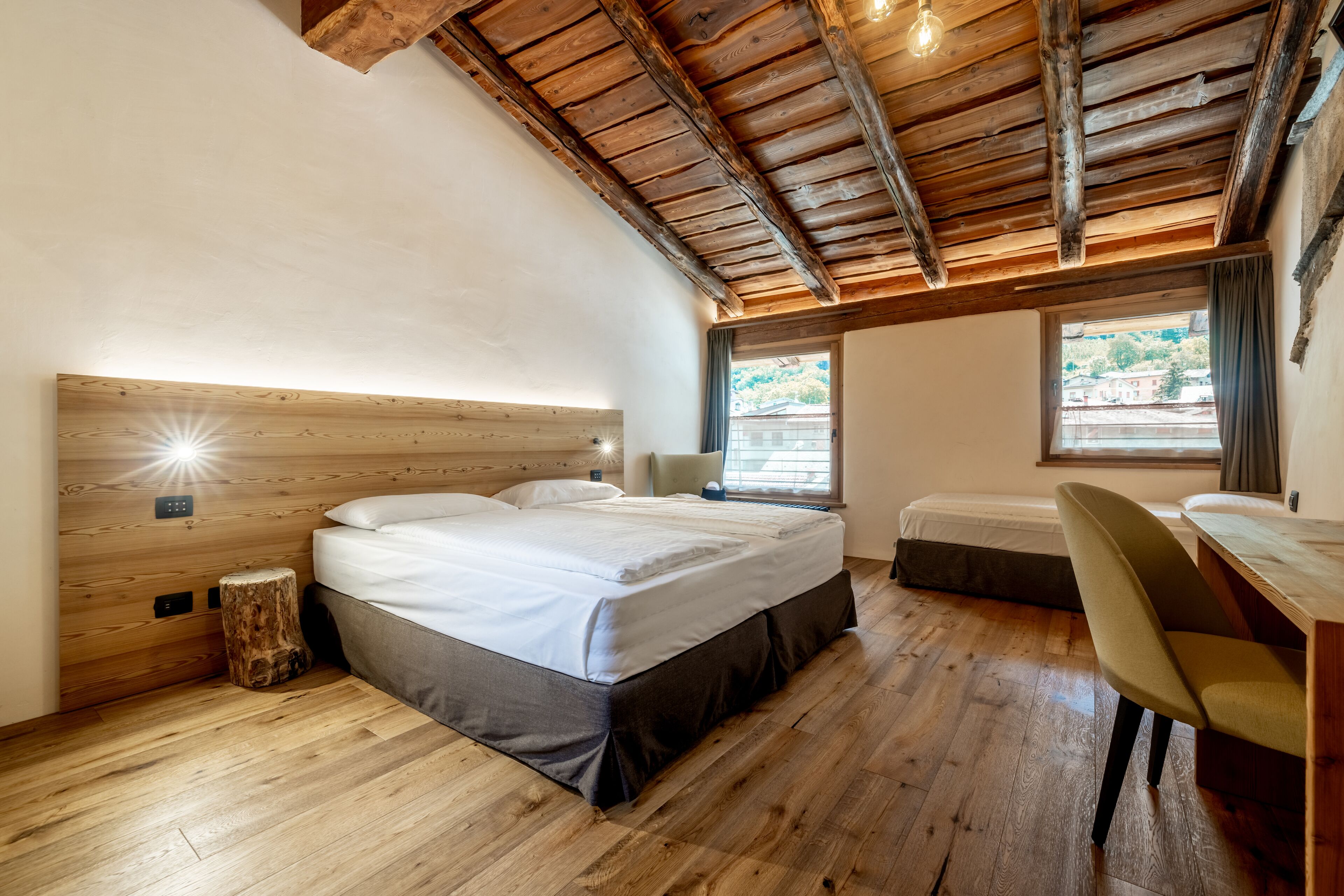 A bedroom with a wooden ceiling, a bed, a desk, and a window with curtains.