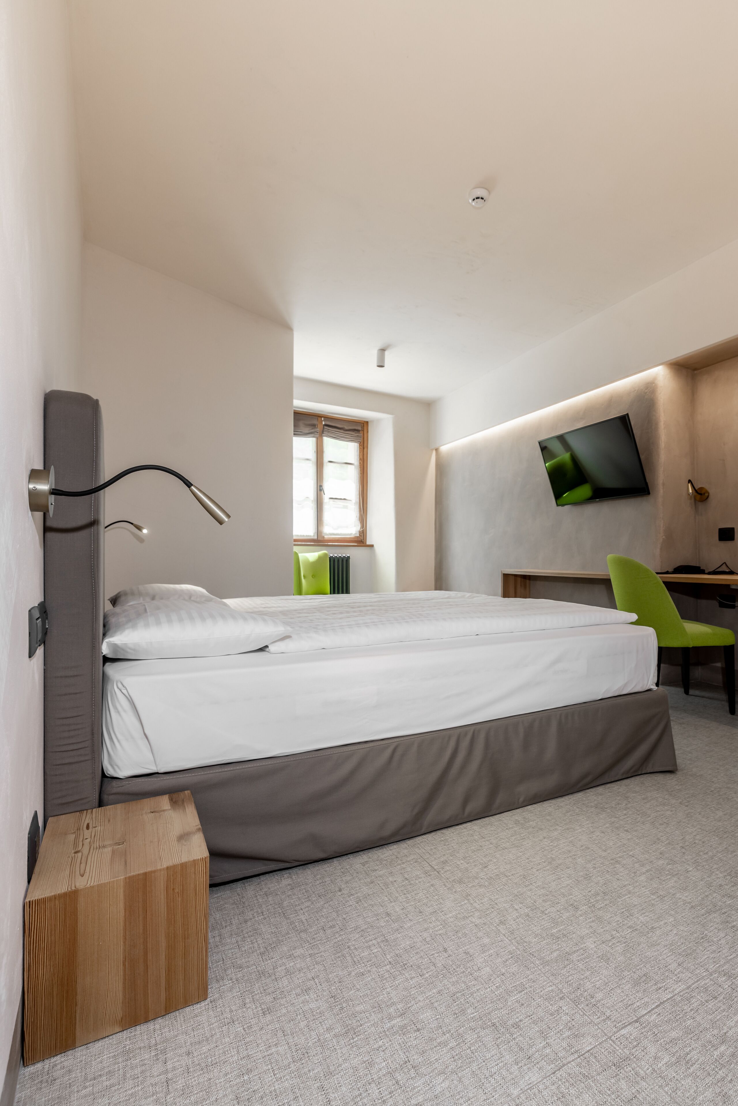 Ein modernes Hotelzimmer mit einem Bett, einem Schreibtisch, einem Sessel und einem an der Wand befestigten Fernseher.