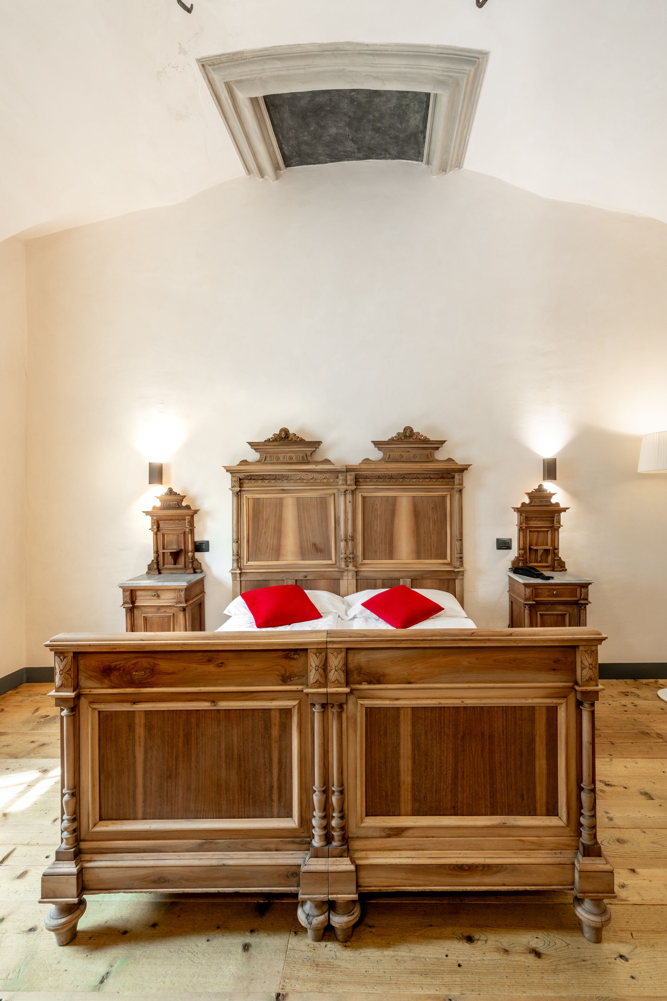 A wooden double bed with a headboard, two bedside tables, and a nightstand with a lamp.