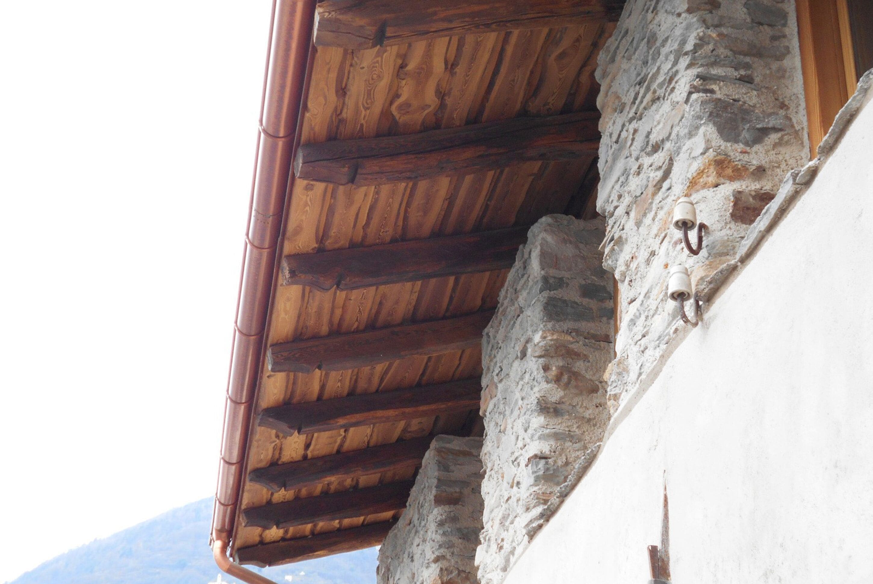 A rustic stone wall with a wooden roof structure.