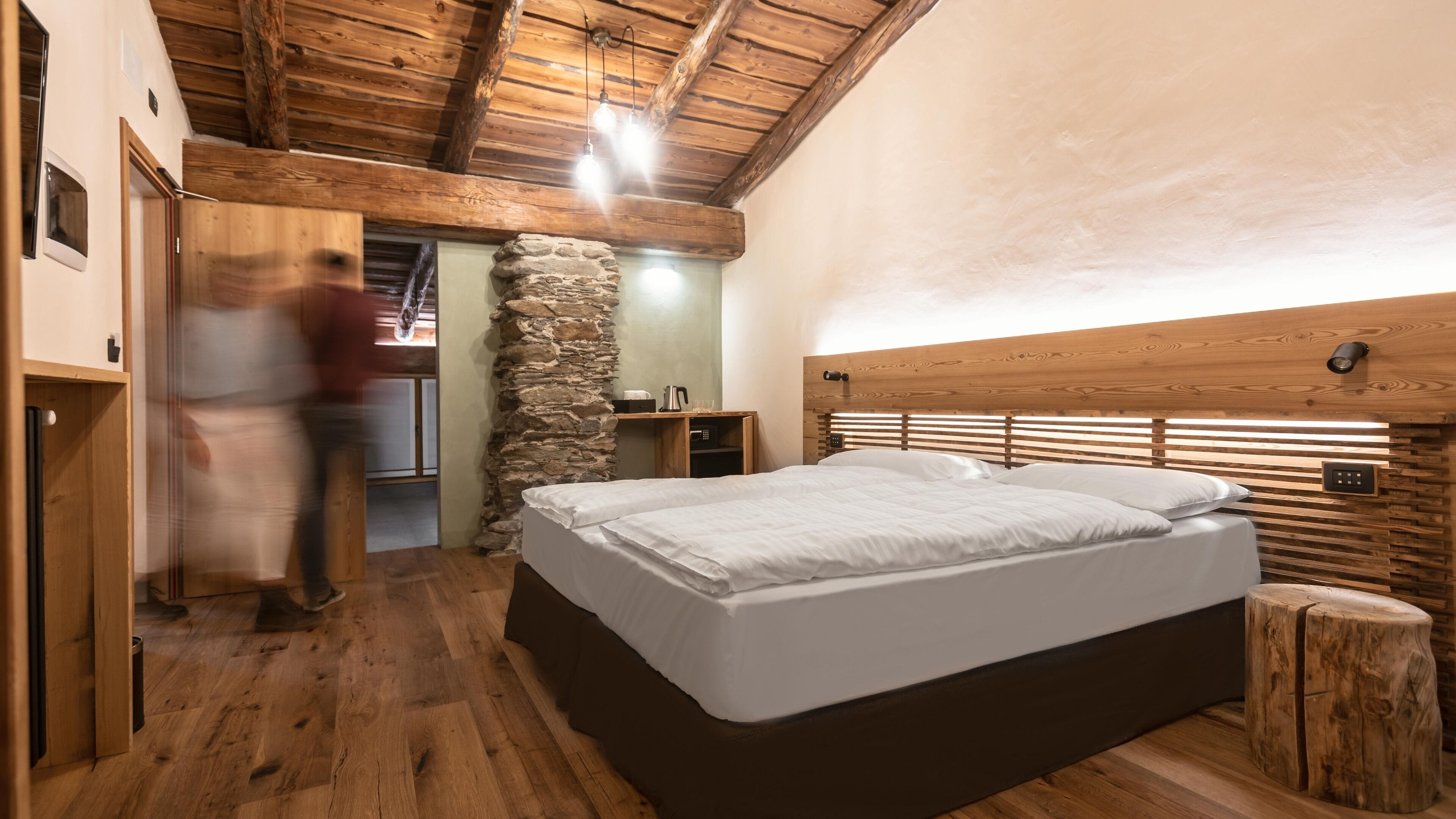 Un dormitorio con cabecera de madera, pared de piedra y cama con ropa blanca.
