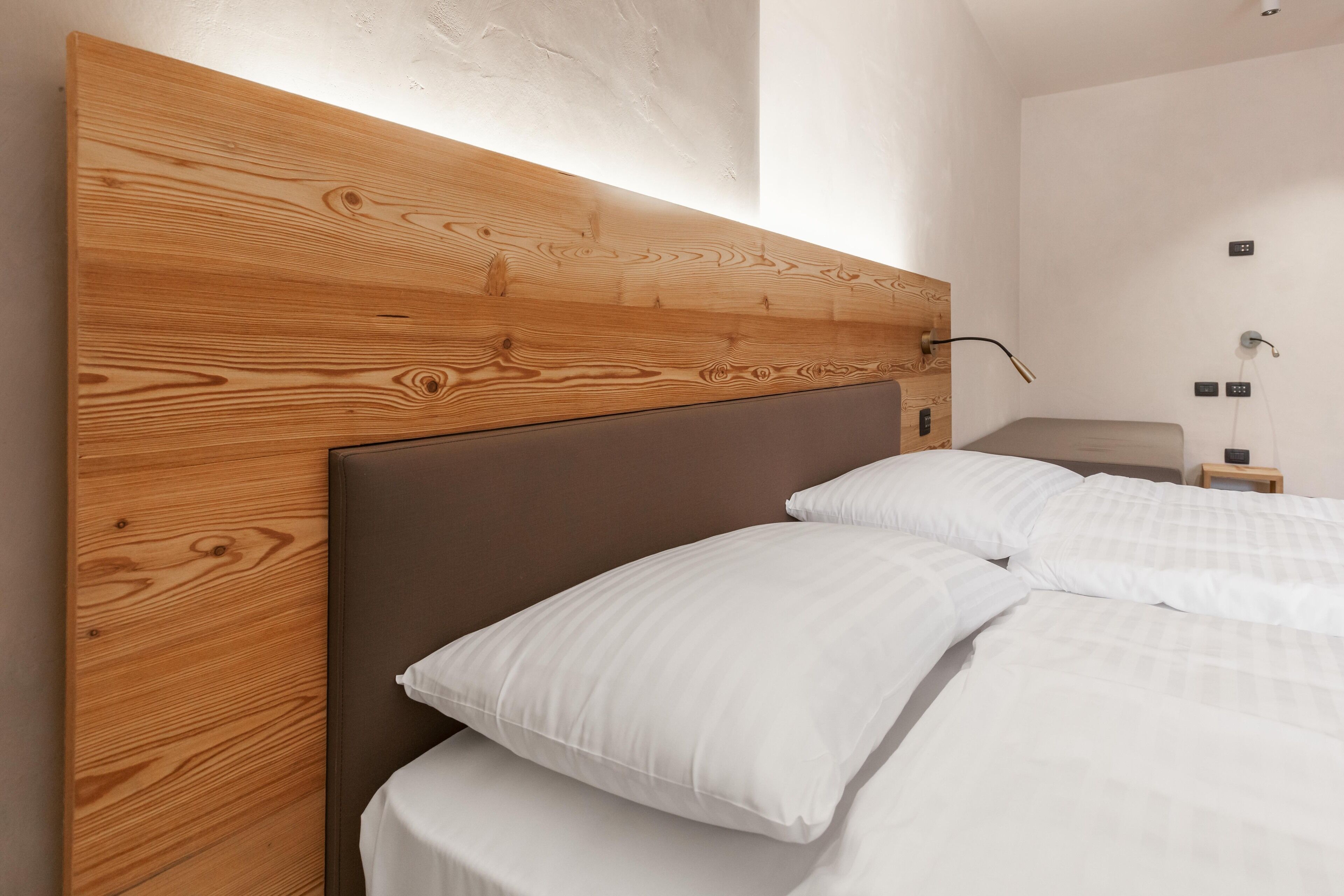 A modern bedroom with a wooden headboard, white bedding, and a bedside table with a lamp.