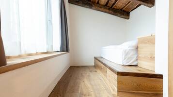 Un dormitorio con piso de madera, una cama con ropa blanca, una ventana con cortinas y un techo de madera.