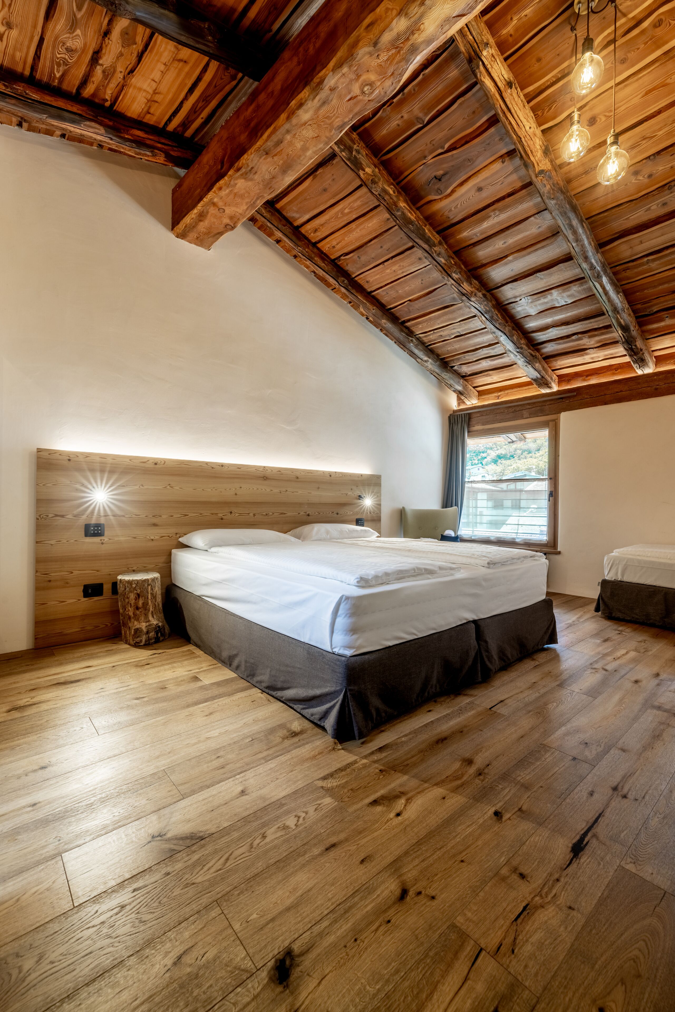A bedroom with a wooden ceiling, a large bed, a bedside table, and a window with a view.