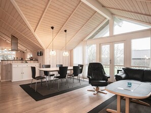 Ampla sala de estar com mesa e cadeiras para refeições, um sofá de couro preto e uma grande janela com vista para o exterior.