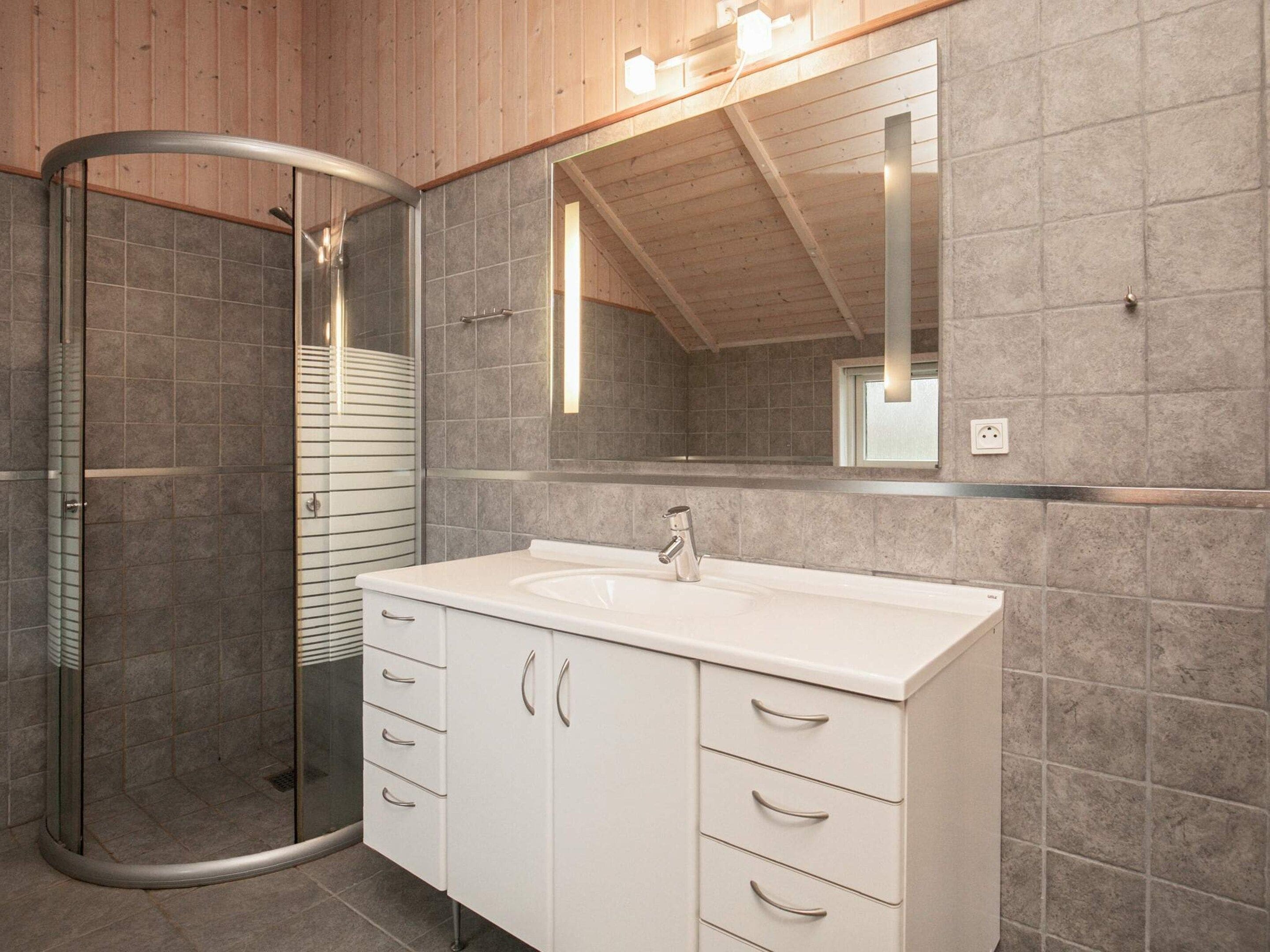 Un baño moderno con cabina de ducha de vidrio, tocador blanco con lavamanos y un espejo grande.